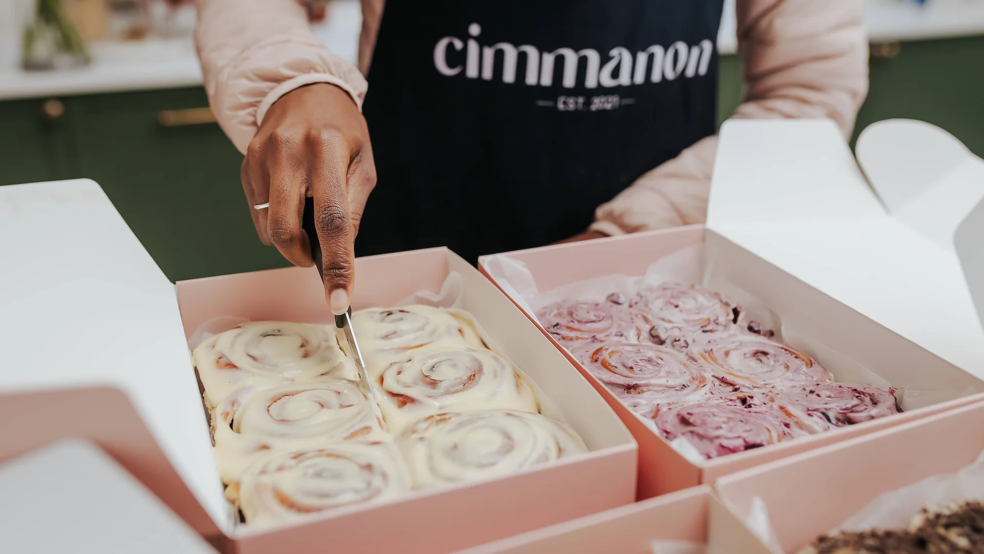 Hands cutting freshly baked Cimmanon cinnamon rolls from open boxes
